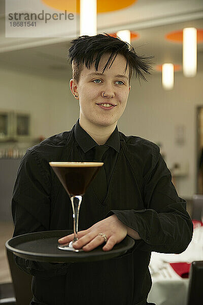 Lächelnder junger Barkeeper serviert Cocktail
