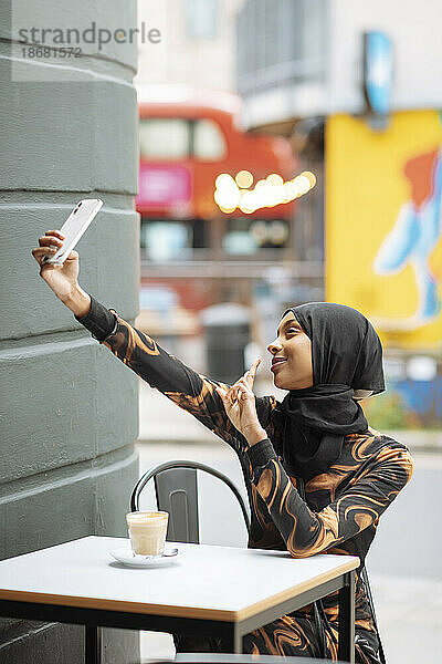 Junge Frau im Hijab macht ein Selfie im Straßencafé