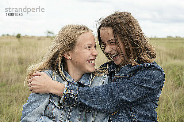 Lächelnde Freundinnen (10-11) umarmen sich im Feld