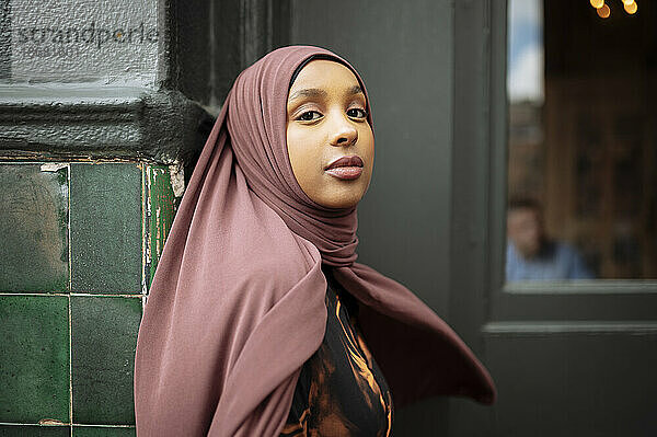 Porträt einer jungen Frau im Hijab  die sich an ein Gebäude lehnt