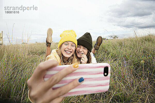 Lächelnde Freundinnen (10-11) liegen im Gras und machen ein Selfie
