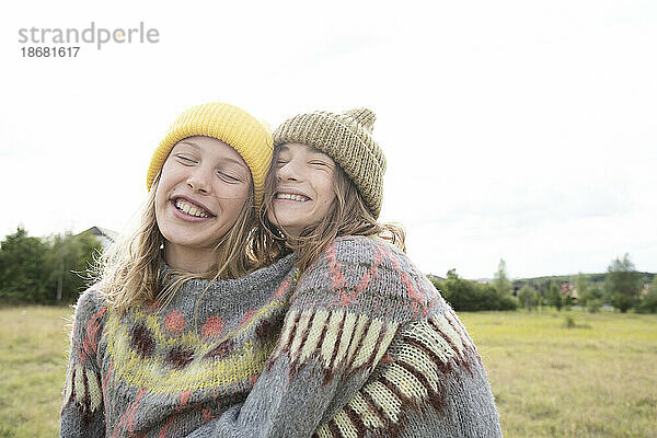 Lächelnde Freundinnen (10-11) tragen einen Pullover auf dem Feld