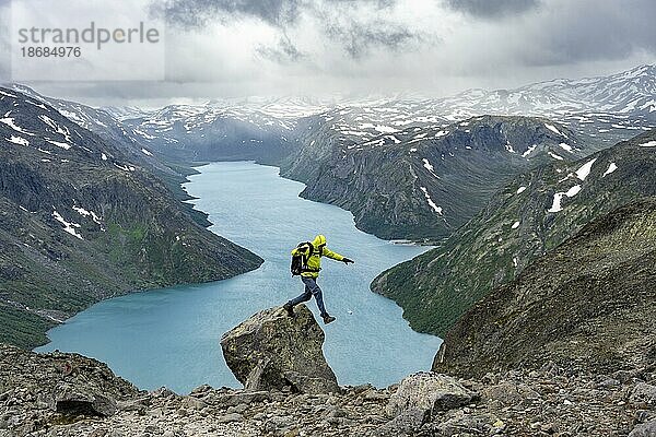 Bergsteiger springt von Felsen  Besseggen Wanderung  Gratwanderung  Ausblick auf See Gjende und verschneite Berge  Jotunheimen Nationalpark  Vågå  Innlandet  Norwegen  Europa