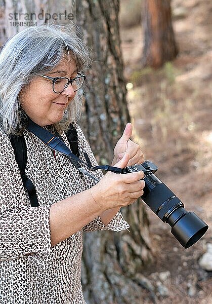Weißhaarige  bebrillte Fotografin lächelt  während sie die Fotos auf ihrer Kamera mit einem zustimmenden Nicken betrachtet