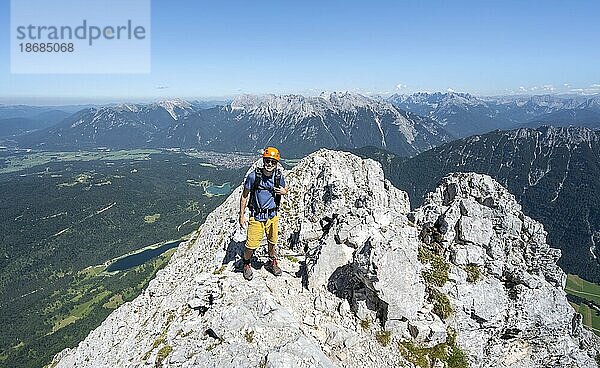 Bergsteiger klettert im Fels  beim Aufstieg zur Oberen Wettersteinspitze  hinten Gipfel des Karwendelgebirge  Wettersteingebirge  Bayerische Alpen  Bayern  Deutschland  Europa