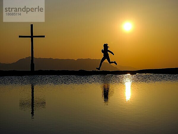 Silhouette einer Läuferin mit Gipfelkreuz bei Sonnenuntergang  Spiegelung im Wasser  Trattberg  Bad Vigaun  Land Salzburg  Österreich  Europa