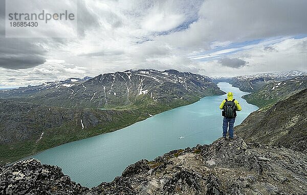 Bergsteiger blickt in die Ferne  Besseggen Wanderung  Gratwanderung  Ausblick auf See Gjende und verschneite Berge  Jotunheimen Nationalpark  Vågå  Innlandet  Norwegen  Europa