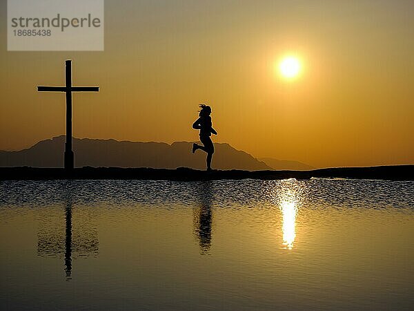 Silhouette einer Läuferin mit Gipfelkreuz bei Sonnenuntergang  Spiegelung im Wasser  Trattberg  Bad Vigaun  Land Salzburg  Österreich  Europa