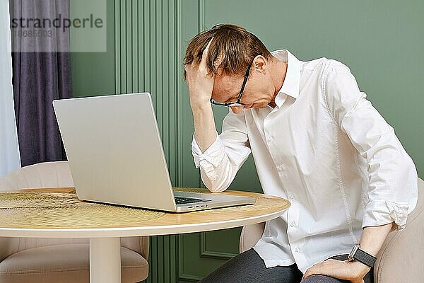 Aufgeregter und müder Mann mittleren Alters mit Laptop senkt den Kopf