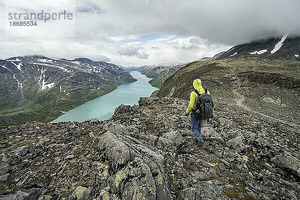 Bergsteiger auf steinigem Wanderweg  Besseggen Wanderung  Gratwanderung  Ausblick auf See Gjende und verschneite Berge  Jotunheimen Nationalpark  Vågå  Innlandet  Norwegen  Europa