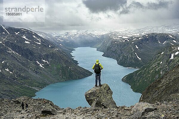 Bergsteiger steht auf Felsen  Besseggen Wanderung  Gratwanderung  Ausblick auf See Gjende und verschneite Berge  Jotunheimen Nationalpark  Vågå  Innlandet  Norwegen  Europa