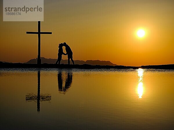 Paar küsst sich neben Gipfelkreuz bei Sonnenuntergang  Silhouette  Spiegelung im Wasser  Trattberg  Bad Vigaun  Land Salzburg  Österreich  Europa