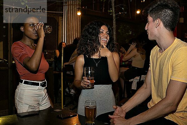 Drei freundliche  gemischtrassige Menschen trinken Bier in einer Bar. Multiethnisches Konzept