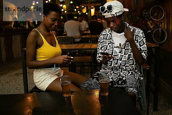 Junges Afro Paar  das sich in einer Bar ignoriert  während es Mobiltelefone benutzt
