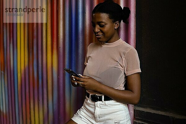 Glückliche schwarze Frau mit Smartphone und lächelnd auf buntem Hintergrund