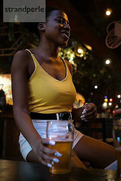 Afrikanische Frau in Kneipe versammelt  genießen angenehmes Gespräch mit einem Bierglas in gemütlicher Atmosphäre