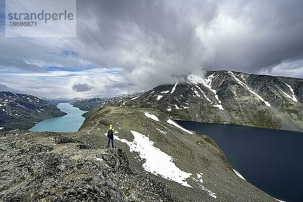 Bergsteiger auf steinigem Wanderweg  Besseggen Wanderung  Gratwanderung  Ausblick auf See Gjende  See Bessvatnet und verschneite Berge  Jotunheimen Nationalpark  Vågå  Innlandet  Norwegen  Europa