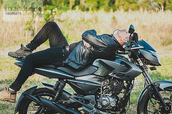 Motorradfahrer in Jacke auf seinem Motorrad liegend in der Natur. Biker Mann liegend auf seinem Motorrad im Freien