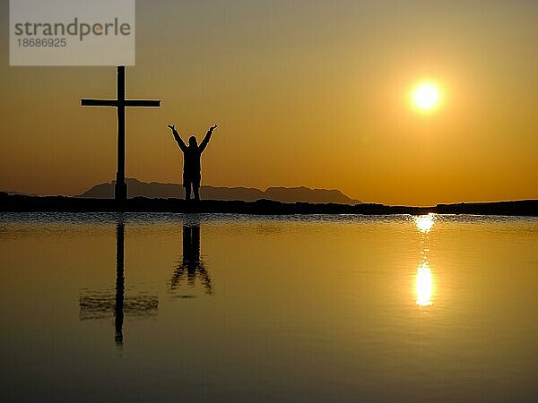 Silhouette einer Frau mit hochgestreckten Armen neben Gipfelkreuz bei Sonnenuntergang  Spiegelung im Wasser  Trattberg  Bad Vigaun  Land Salzburg  Österreich  Europa