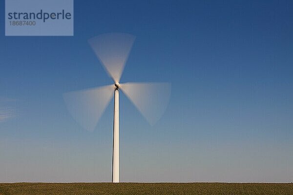Sich drehende Rotorblätter einer Windkraftanlage im Feld vor blauem Himmel