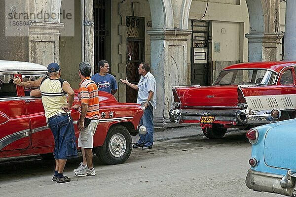 Kubanische Männer diskutieren auf der Straße und rote alte 1950er Jahre Oldtimer  Yank Tank in Old Havana  La Habana Vieja  Kuba  Karibik  Mittelamerika