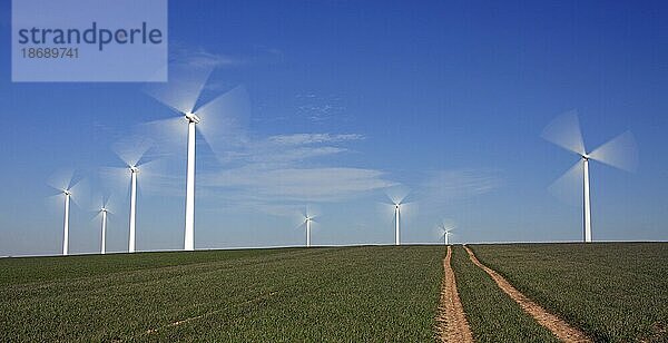 Sich drehende Flügel von Windkraftanlagen in einem Windpark vor blauem Himmel