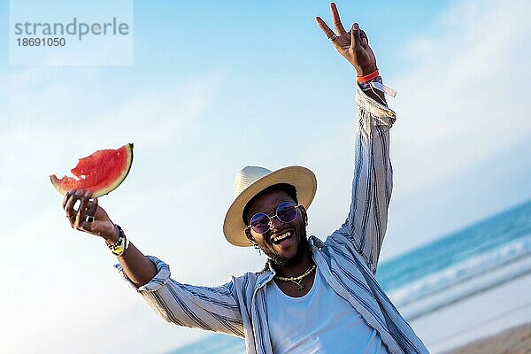 Schwarz ethnischen Mann genießen Sommerurlaub am Strand essen eine Wassermelone Spaß haben