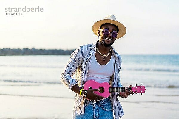 Schwarzer ethnischer Mann spielt Ukulele am Meer und genießt den Sommerurlaub