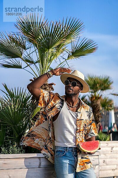 Schwarzer ethnischer Mann genießen Sommerurlaub am Strand  Sombrero und eine Wassermelone