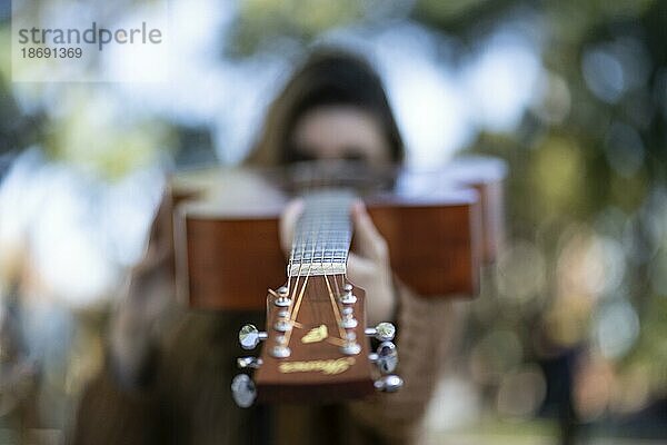 Frau zeigt mit ihrer Gitarre in die Kamera. Inspirierendes Konzept