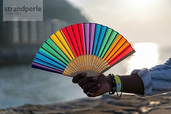 Stolz auf die LGBTQ Gemeinschaft. Hand mit gefälschten Nägeln in den Farben des Regenbogens hält Regenbogenfächer