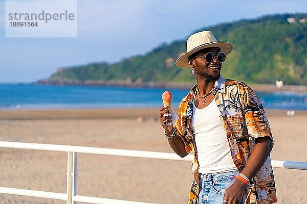 Schwarze ethnische Mann genießen Sommerurlaub am Strand essen ein Eis genießen schlendern