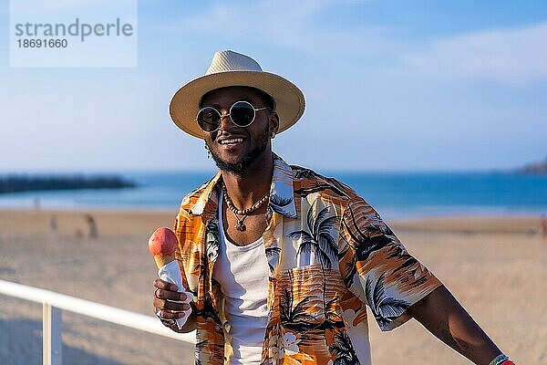 Schwarzer ethnischer Mann genießt Sommerurlaub am Strand und isst Eiscreme
