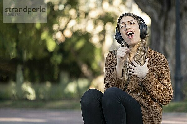 Blonde Frau sitzt auf der Straße  hört Musik und tut so  als hätte sie ein Mikrofon in der Hand und singt