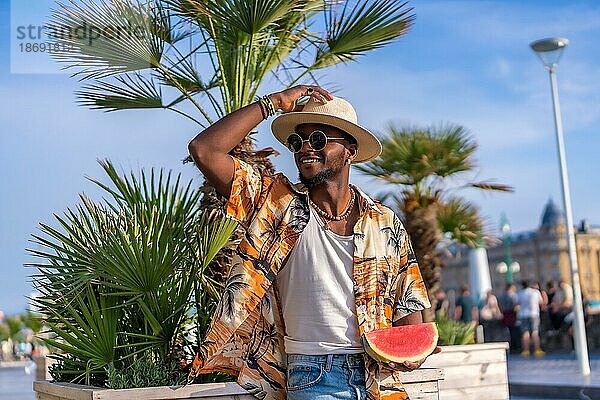 Porträt eines schwarzen ethnischen Mannes genießen Sommerurlaub am Strand  Schatten und eine Wassermelone