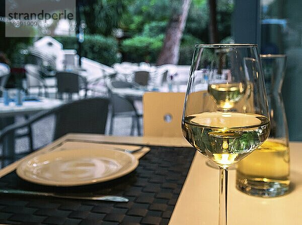 Ein Glas und eine Karaffe Weißwein auf einem Tisch in einem Straßencafé und Geschirr  Geschirr und Besteck  selektiver Fokus und unscharfer Hintergrund. Essen im Freien im Sommer  Urlaub Mahlzeiten  Pause  Mittagszeit  Abendessen