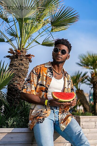 Schwarzer ethnischer Mann genießen Sommerurlaub am Strand mit einer Wassermelone