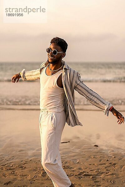 Porträt eines attraktiven schwarzen ethnischen Mannes  der seinen Sommerurlaub am Meer genießt  sich frei fühlt und tanzt