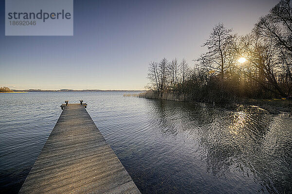 Die tiefstehende Abendsonne scheint auf den verlassenen Badesteg in Pülsen am Nordufer des Selenter Sees