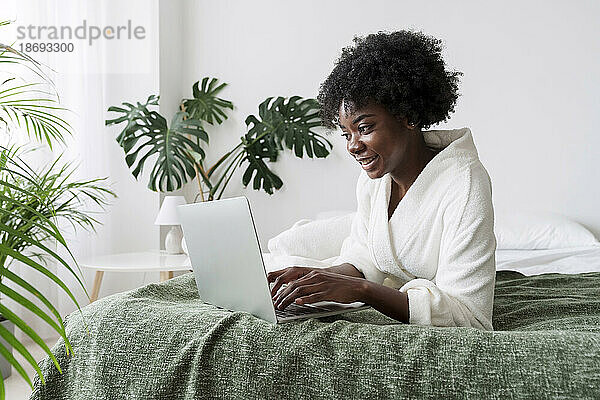 Frau benutzt Laptop und liegt zu Hause im Bett