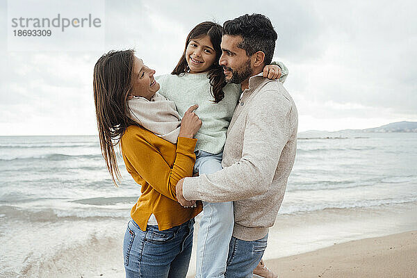 Glückliche Frau steht mit Mann und Tochter an der Küste am Strand