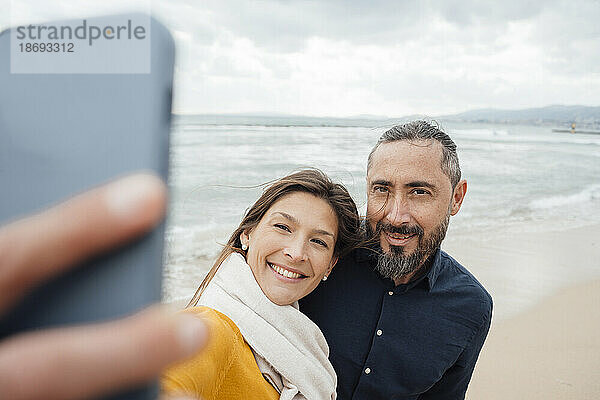 Glückliche Frau  die am Strand ein Selfie mit einem reifen Mann per Mobiltelefon macht