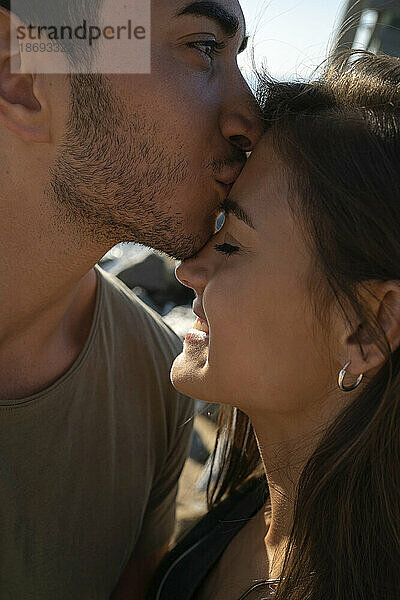 Junger Mann küsst glückliche Frau auf die Stirn