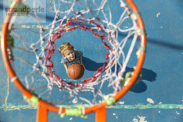 Junge steht mit Basketball unter Korb am Sportplatz