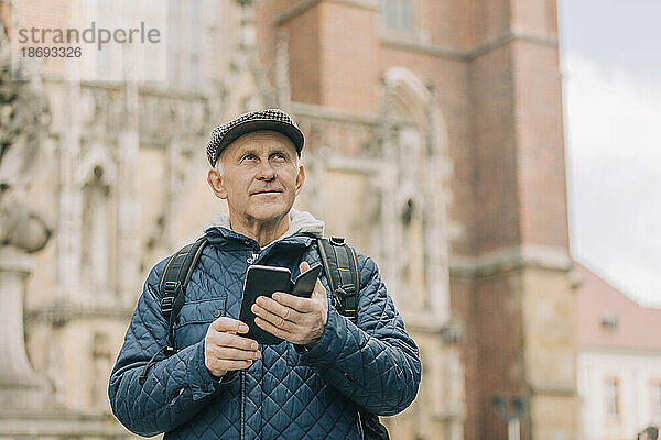 Älterer Mann mit Smartphone steht vor der Kathedrale