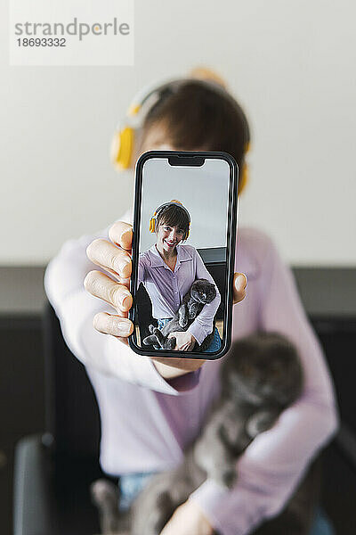 Glückliche Frau mit Headset und Katze  die ein Selfie per Smartphone macht