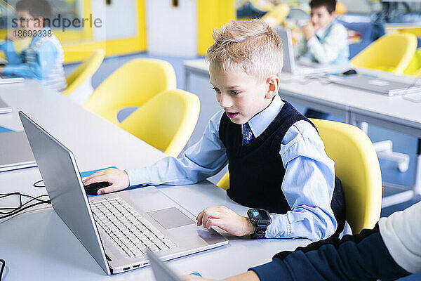Junge mit blonden Haaren benutzt Laptop im Computerunterricht