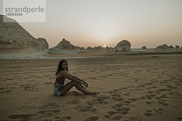Frau sitzt bei Sonnenuntergang auf Sand in der Wüste