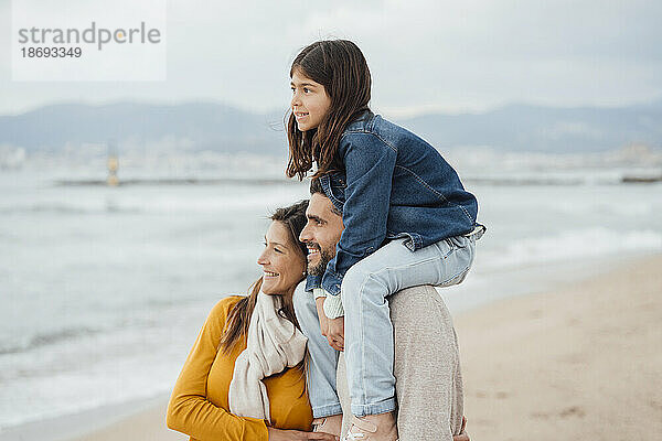 Lächelnder Mann und Frau mit Tochter stehen zusammen am Strand