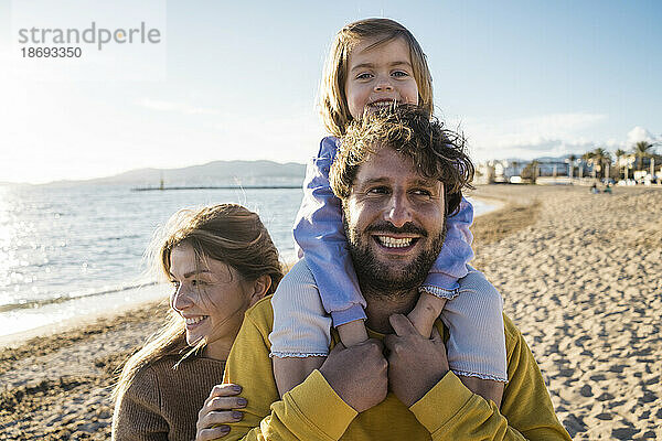 Nettes Mädchen  das von einer Frau am Strand auf den Schultern des Vaters sitzt